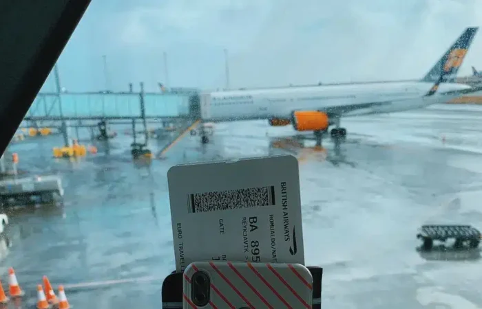 Traveler holding a boarding pass with an airplane visible through an airport window — Portugal Startup Visa physical presence