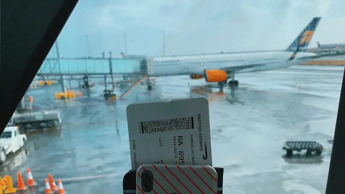 Traveler holding a boarding pass with an airplane visible through an airport window — Portugal Startup Visa physical presence